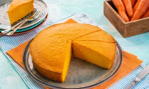 Una soffice torta di carote, appena affettata, su un piatto. Accanto, un piattino con una fetta e delle carote fresche in un cesto.