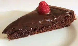 Una fetta di gateau al cioccolato, lucida e golosa, con una fragola fresca in cima, su un piatto bianco.