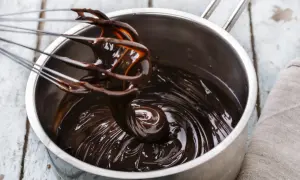 Una frusta mescola una lucida glassa al cioccolato in una pentola d'acciaio.