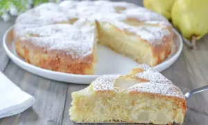 Una fetta di torta pere soffice e profumata, cosparsa di zucchero a velo, su un tavolo di legno.