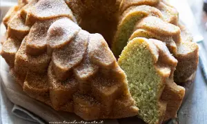 Una deliziosa torta al pistacchio, soffice e profumata, cosparsa di zucchero a velo. La fetta rivela il suo colore verde brillante.