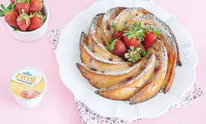 Torta di fragole e yogurt, soffice e profumata, decorata con zucchero a velo e fragole fresche. Accanto, una ciotolina di fragole e un vasetto di yogurt.