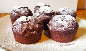 Cinque muffin al cioccolato senza burro, spolverati di zucchero a velo, su un piatto chiaro.