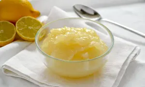 Una ciotola di cremosa crema al limone, con limoni freschi affettati sullo sfondo.