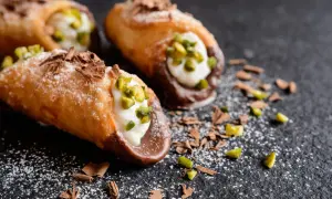 Cannoli siciliani con la loro deliziosa farcitura, guarniti con pistacchi e scaglie di cioccolato su fondo scuro.