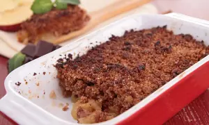 Crumble cacao appena sfornato in una teglia rossa, con mele e cioccolato a lato.