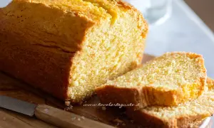 Plumcake senza yogurt dorato e soffice, tagliato a fette su un tagliere di legno con un coltello.
