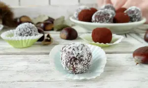 Deliziosi tartufini di castagne, alcuni ricoperti di cocco, altri di cacao, su un tavolo di legno con castagne sparse.