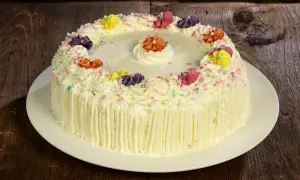 Torta compleanno uomo con panna, decorata con fiori colorati e codette, pronta per festeggiare.