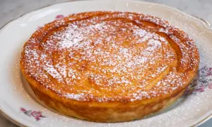 Migliaccio napoletano ricetta della nonna, dorato e cosparso di zucchero a velo, su un piatto decorato.