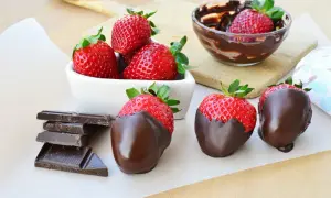 Fragole fresche e succose, alcune immerse in cioccolato fuso, altre pronte per esserlo, accanto a tavolette di cioccolato fondente.