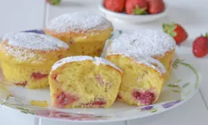 Morbidi muffin alle fragole, spolverati di zucchero a velo, invitano a un dolce assaggio. Pezzi di fragola succosa si intravedono nell'impasto soffice.