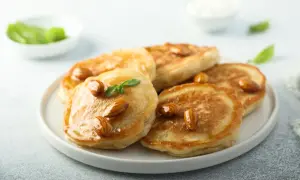 Pancakes con farina di mandorle, guarniti con mandorle intere e sciroppo dorato, su un piatto bianco.