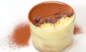 Delizioso tiramisù con crema pasticcera, cacao e scaglie di cioccolato in un bicchiere.