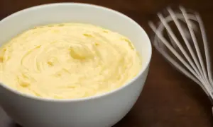 Crema pasticcera senza glutine, liscia e vellutata, pronta per farcire dolci. Vicino, una frusta in movimento.