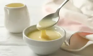 Latte condensato bimby versato da un cucchiaio in una ciotola bianca. Dolcezza cremosa pronta per dolci e caffè.