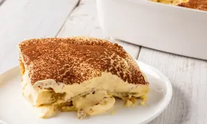 Una fetta di tiramisù, un classico dolce con mascarpone, cosparso di cacao amaro, su un piatto bianco.