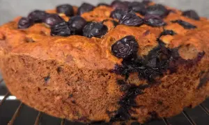 Torta senza zucchero con mirtilli, dorata e soffice, appena sfornata e adagiata su una griglia.