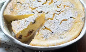 Torta soffice ricotta e cioccolato, cosparsa di zucchero a velo, in una tortiera. Una fetta è già stata tagliata.