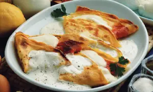 Crepes ripiene di prosciutto e formaggio, condite con una salsa cremosa. Una deliziosa panna acida ricetta per un piatto unico.