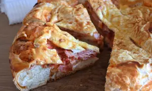 Una torta rustica con pasta sfoglia ripiena di salumi e pomodoro, tagliata a fette su un tagliere di legno.