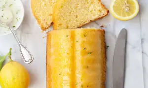 Un delizioso plumcake al limone glassato, con fette affettate, limoni freschi, una ciotolina di glassa e un coltello.