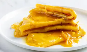 Pila di crepes suzette dorate, ricoperte da una salsa all'arancia lucida e invitante.