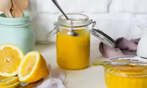 Vasetto di vetro pieno di lemon curd, con limoni freschi affettati e un cucchiaino.