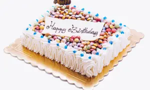Torta rettangolare con glassa bianca, decorata con tanti smarties colorati e la scritta "Happy Birthday".