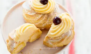 Zeppole di San Giuseppe, dolci soffici con crema pasticcera e ciliegina, uno è tagliato per mostrarne l'interno goloso.