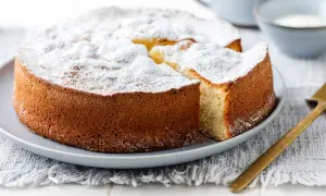 Una soffice torta allo yogurt, cosparsa di zucchero a velo, attende di essere gustata. Una fetta è già stata tagliata, rivelando il suo interno invitante.