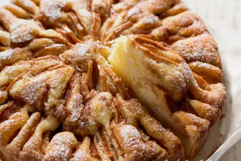 Una deliziosa torta di mele, cosparsa di zucchero a velo, con una fetta appena tolta che rivela la morbidezza dell'impasto e le mele caramellate.