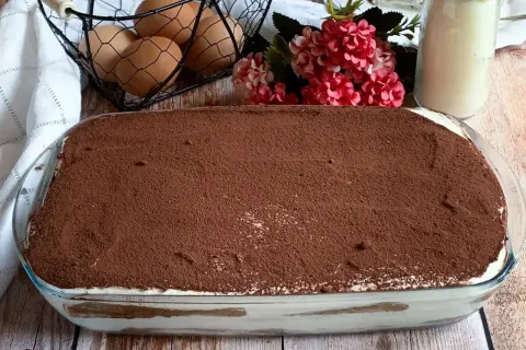 Tiramisù pronto, con 500 g di mascarpone, pronto per essere gustato. Ingredienti freschi come uova e fiori decorano la tavola.