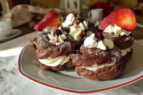 Zeppole al cacao con panna montata, ciliegie e fragole, spolverate di zucchero a velo.