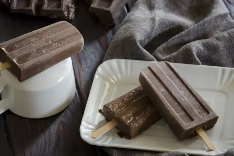 Tre ghiaccioli al cioccolato, uno su una tazza bianca, gli altri su un piatto, con pezzi di cioccolato sullo sfondo.
