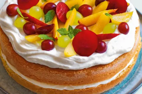 Torta con pan di spagna, panna montata e frutta fresca: uva, pesche e prugne. Un dolce estivo colorato e invitante.