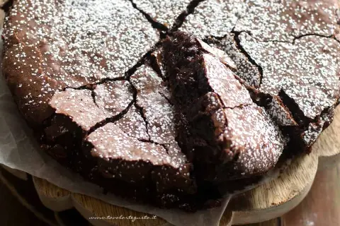 Deliziosi dolci con cioccolato fondente, una torta scura e umida con una crosta screpolata e cosparsa di zucchero a velo.