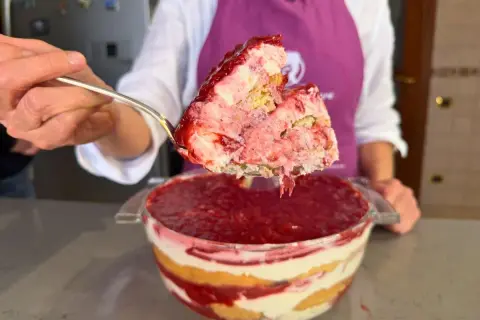 Un cucchiaio solleva una porzione generosa di tiramisù alle fragole, mostrando strati cremosi e succosi.