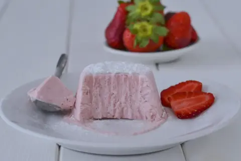 Delizioso semifreddo alle fragole, con una porzione su un cucchiaio e fragole fresche sullo sfondo.