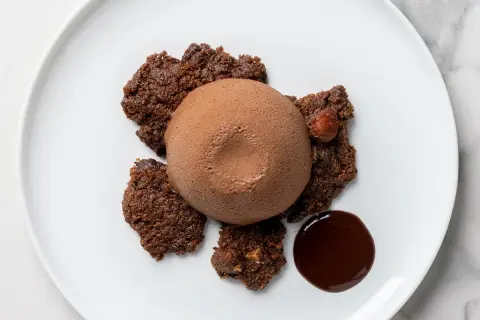 Delizioso semifreddo al cioccolato su un piatto bianco, circondato da croccanti biscotti al cacao e una goccia di salsa al cioccolato.