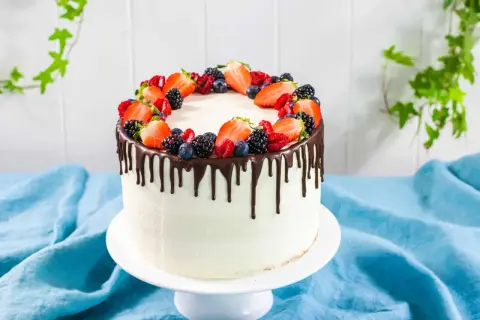 Torta bianca con glassa al cioccolato che cola, decorata con fragole, mirtilli e lamponi freschi. Un drip cake perfetto per ogni occasione.