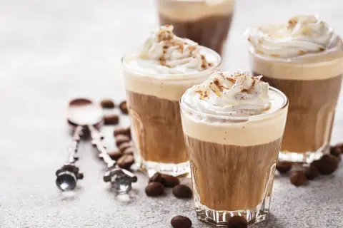 Tre bicchieri di deliziosa crema al caffè, guarniti con panna montata e cacao, circondati da chicchi di caffè.