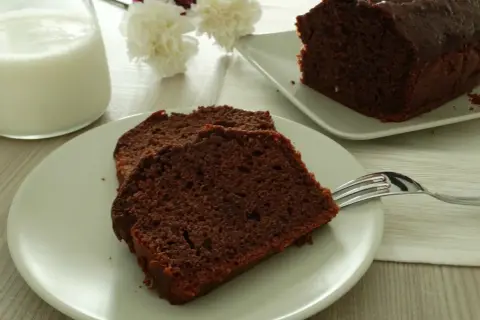Fette di plumcake yogurt e cioccolato su un piatto, con una forchetta e un bicchiere di latte.