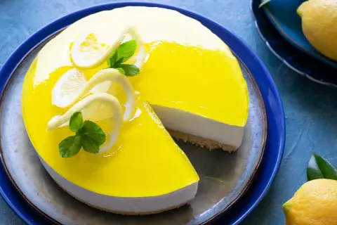 Cheesecake lime lucido con decorazioni di limone e menta, una fetta è stata tolta.