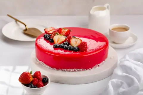 Torta rossa con glassa a specchio, decorata con fragole, mirtilli e lamponi. Un'opera d'arte culinaria.