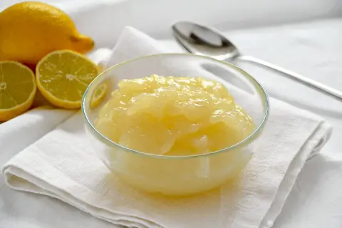 Una ciotola di cremosa crema al limone, con limoni freschi affettati sullo sfondo.