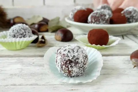 Deliziosi tartufini di castagne, alcuni ricoperti di cocco, altri di cacao, su un tavolo di legno con castagne sparse.