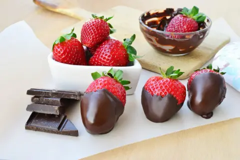 Fragole fresche e succose, alcune immerse in cioccolato fuso, altre pronte per esserlo, accanto a tavolette di cioccolato fondente.