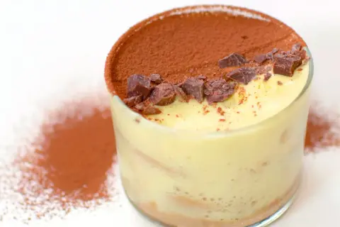 Delizioso tiramisù con crema pasticcera, cacao e scaglie di cioccolato in un bicchiere.