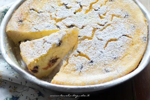 Torta soffice ricotta e cioccolato, cosparsa di zucchero a velo, in una tortiera. Una fetta è già stata tagliata.